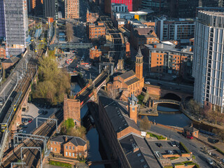 Aerial image of Manchester, UK, on a sunny day showing red brick buildings, canals, modern...
