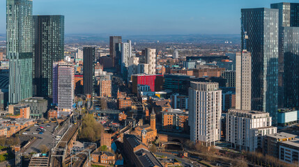 Aerial view of Manchester, UK, showcasing skyscrapers like Beetham Tower, railway tracks, canals, and a mix of modern and historic architecture.