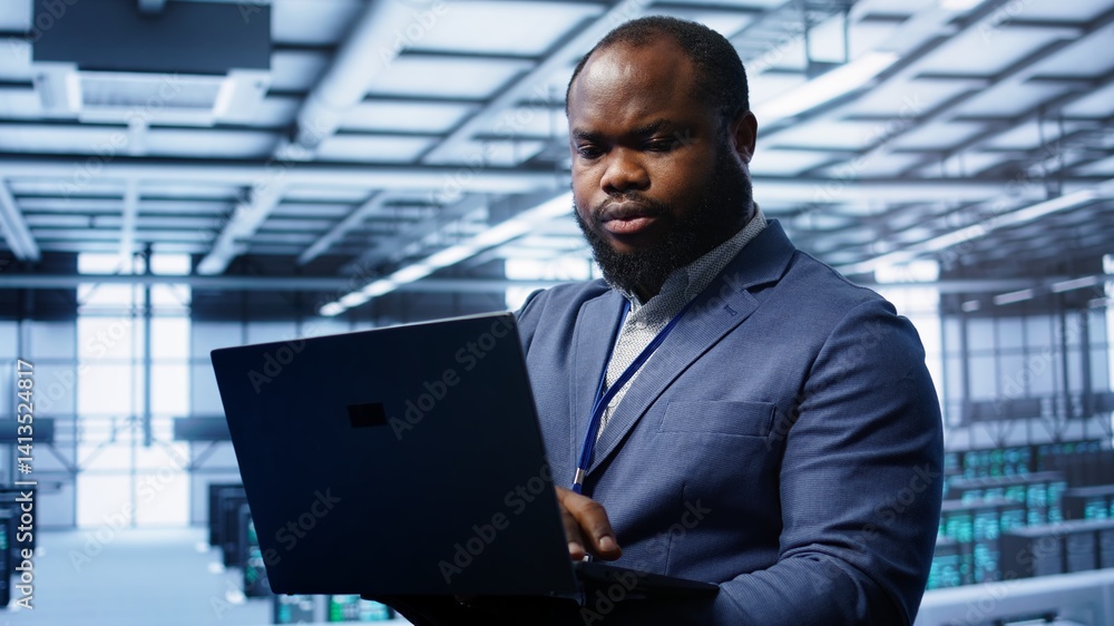 Poster computer scientist in high tech facility using laptop to patch network issues affecting server cabin