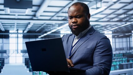 Computer scientist in high tech facility using laptop to patch network issues affecting server...