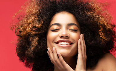 Beautiful dark-skinned curly-haired girl with closed eyes and hands near her face.