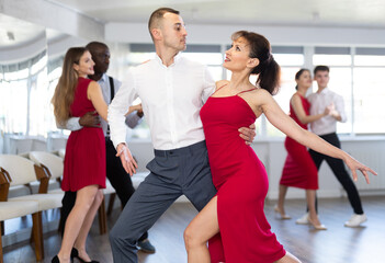 Smiling young woman in red dress and her partner successfully perform mesmerizing movements of paso doble dance during dance party