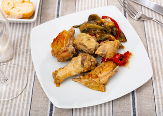Chicken wings and thighs served with stewed vegetables on a white square plate in the cafeteria