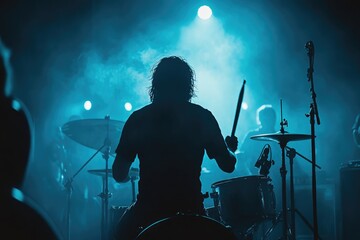Silhouetted drummer performing on stage, illuminated by blue stage lights during a concert.