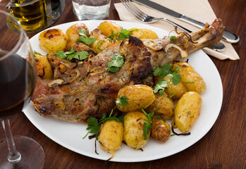 Baked lamb leg served with new potatoes and parsley..Delicious baked lamb leg served with whole baked potatoes and garnished with parsley..Appetizing lamb leg with baked new potatoes, served on white