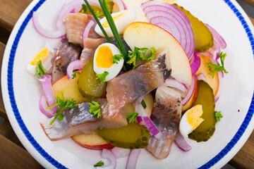 Salad Herring with apples, pickles, onion and quail egg served on plate