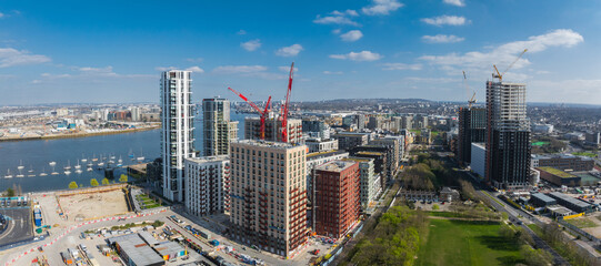 Aerial view of London's urban area with high rise buildings, construction cranes, the River Thames on the left, and a green park in the foreground. © Aerial Film Studio