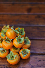Heap of orange persimmon lies on an old wooden table. Cropped