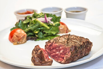 Grilled beef steak with lettuce salad and spicy sauces, plate of sliced ​​roast beef with salad and tomato on a white background