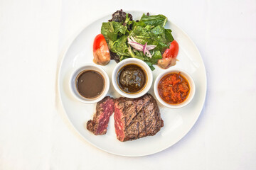 Grilled beef steak with lettuce salad and spicy sauces, plate of sliced ​​roast beef with salad and tomato on a white background