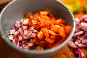 a close-up of a bowl with chopped tomatoes and chopped red onions with black pepper in a gray bowl on a cutting board