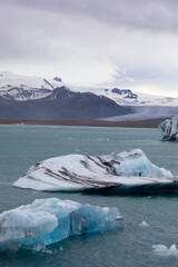 vertical landscape of glaciers in a lagoon in Iceland with snow covered mountains in the background