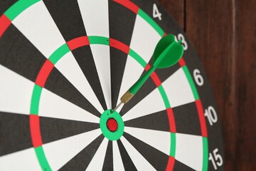 Dart board with arrow on wooden background, closeup