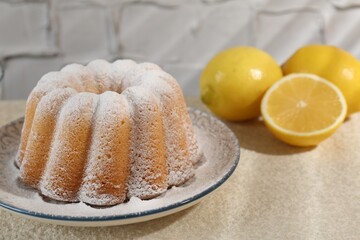 Delicious lemon cake with powdered sugar and citrus fruits on light table against textured wall, closeup