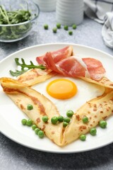 Delicious crepe with egg, bacon, arugula and green peas on grey table, closeup