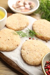 Many uncooked patties and spices on wooden table, closeup