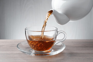 Pouring freshly brewed tea from teapot into cup at wooden table, closeup