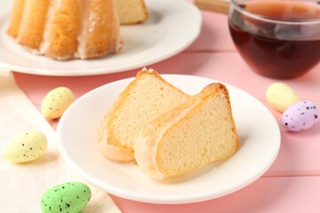 Pieces of delicious bundt cake, Easter eggs and tea on pink wooden table, closeup