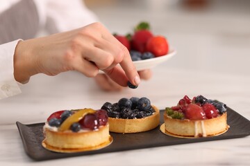 Confectioner decorating tart with blueberry at table, closeup