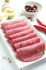 Slices of tasty smoked sausage, spices and olives on white wooden table, closeup