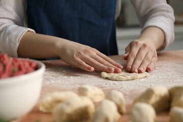 Making khinkali. Woman shaping piece of dough at table in kitchen, closeup