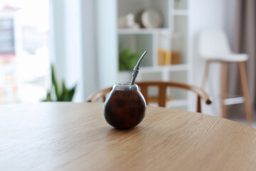 Calabash with mate tea and bombilla on wooden table at home