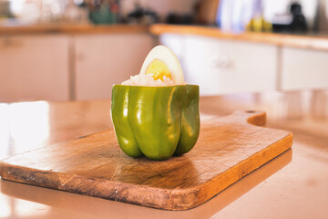 Green bell pepper stuffed with rice, garnished with boiled egg slice, resting on wooden cutting board in home kitchen setting