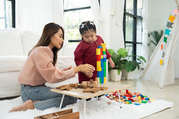 Cherry young mother plays colorful toy block with her Down syndrome daughter,  colorful wooden toys...