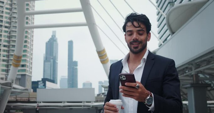 Manager stands on street with mobile phone and coffee. Man is holding phone and typing messages while taking break to look around buildings. Phone is not released from hands of attribute businessman.