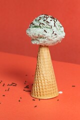 Upside down sugar cone with mint chip ice cream on the top and chocolate sprinkles with an orange background