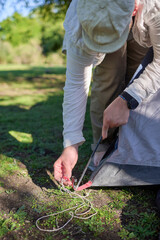 Unrecognizable man putting up the poles of his tent, in the process of setting it up outdoors.