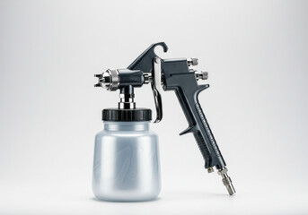 Silver and black air spray gun with attached canister isolated on gray background, commonly used in automotive, furniture, and industrial applications for smooth and even paint coating