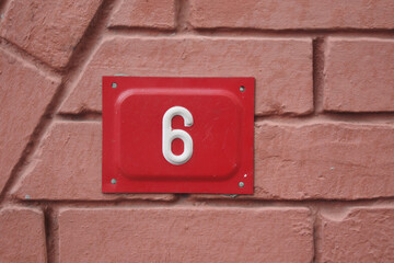 Bright red house number six mounted on textured wall