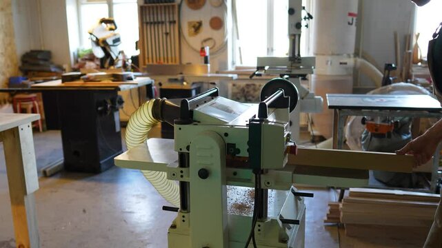 Carpenter craftsman load wooden board into jointer machine. Tool enables smooth planing, reducing splintering on knots and reversing grain. Precise thickness in planing for woodworking projects