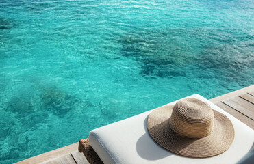 Sun hat and lounge chair offer serene moment, inviting relaxation by tranquil ocean. scene is peaceful and calm