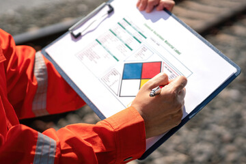 Close-up at safety supervisor's hand during writing on chemical safety checklist to verify the...