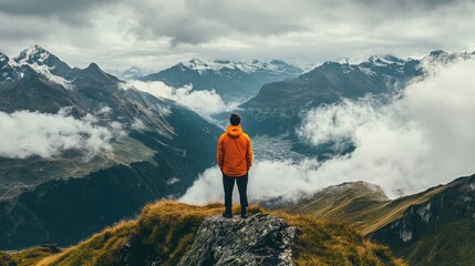 A person in an orange jacket overlooking a breathtaking mountain range with rolling clouds