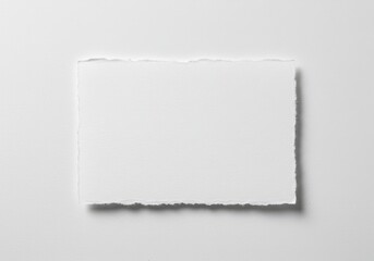 Naklejka premium A torn piece of white paper with a rough edge on a white surface casting a soft shadow beneath it
