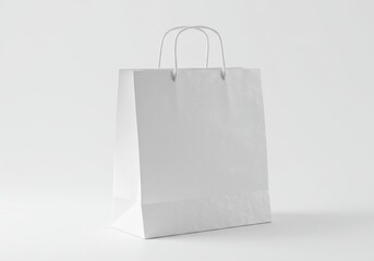 A simple white paper shopping bag with handles standing on a white surface in a bright setting