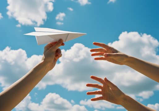 A hand holding a paper airplane with outstretched hands against a blue sky with white clouds