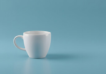 Fototapeta premium White Coffee Mug on Blue Background Minimalist Drinkware Concept, Empty Cup for Beverages and Morning Rituals.
