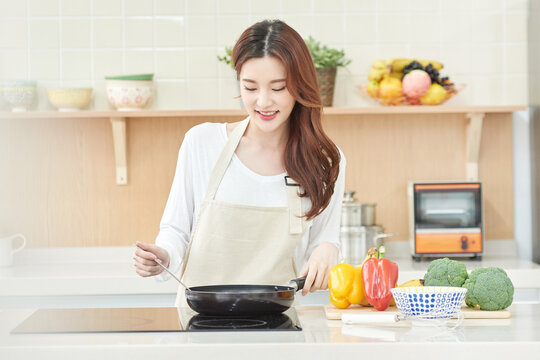 Smiling Asian Woman Cooking with Fresh Vegetables in Modern Kitchen