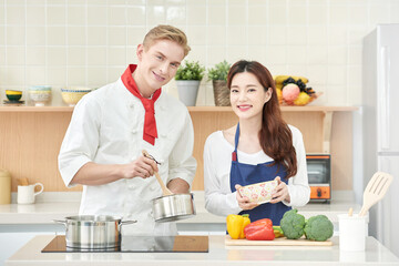 Beautiful Asian Woman in Apron and Caucasian Male Chef Cooking Together in Modern Kitchen