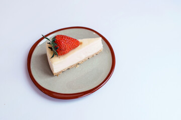 Homemade dessert bakery cafe. Sliced classical plain New York cheesecake with fresh strawberry in vintage style ceramic plate on table with white background.
