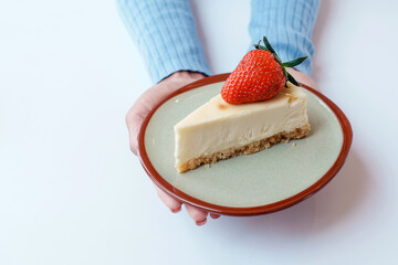 Homemade dessert bakery cafe. Hands of woman holding sliced classical plain New York cheesecake with fresh strawberry in vintage style ceramic plate on table with white background.