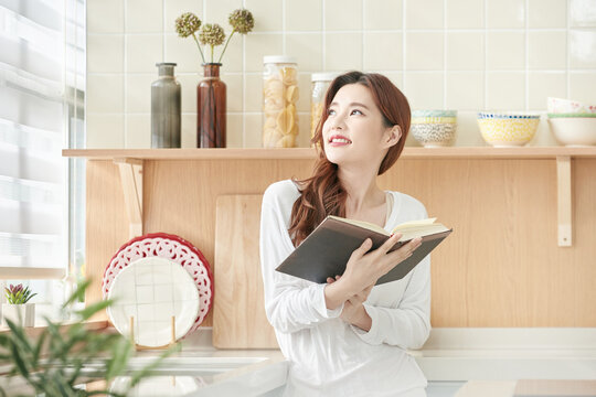 Young Woman Reading Book in Bright Modern Kitchen - Powered by Adobe
