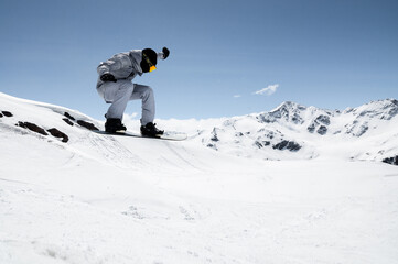 athlete man performing tricks on snowboard, exuding confidence and control in vibrant winter gear against clear skies and alpine scenery. Concept of extreme sport, ski-resort, holidays