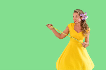 Woman in yellow dress holding measuring tape in a vibrant green setting while showcasing fashion...