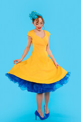 Cheerful woman twirls in a vibrant yellow dress with blue accents against a bright blue background