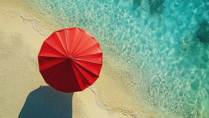 Red beach umbrella on sandy shore next to turquoise water